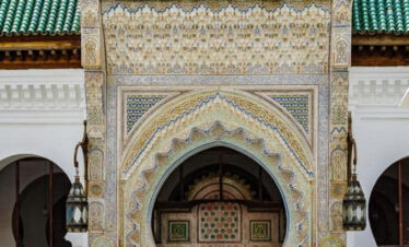"Scenic camel caravan in the Sahara Desert during a 3-day tour from Fes to Marrakech, with desert camp and mountain landscapes in the background.
